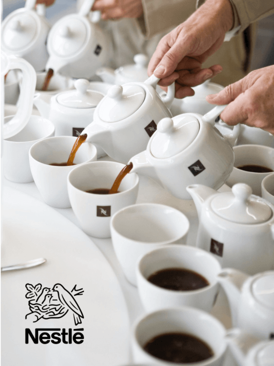 Multiple white teapots pouring coffee into teacups with the Nestle logo overlayed.